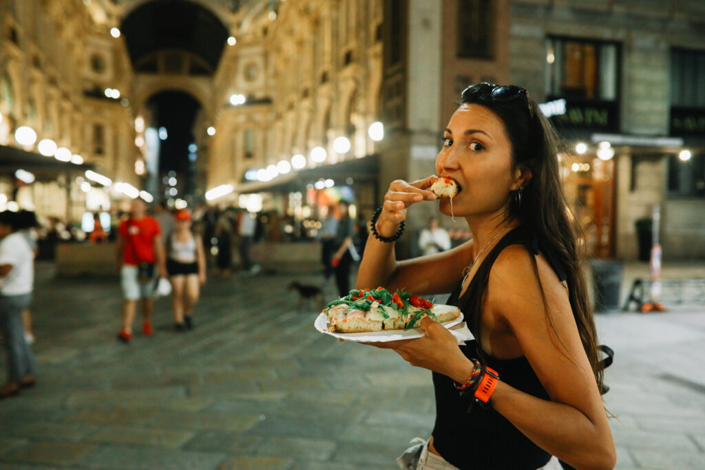 Woman having a pizza slice on the go on the streets of Milano, Italy, in the evening.